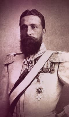 Prince Alexander of Battenberg. He has wavy dark brown hair, a full beard, and is wearing a military uniform.