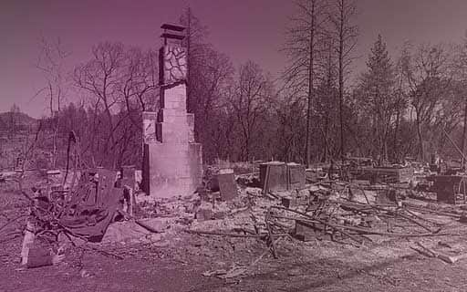 A home destroyed by fire. Only the chimney is left standing, still partially covered at the top by its decorative rock sheeting.