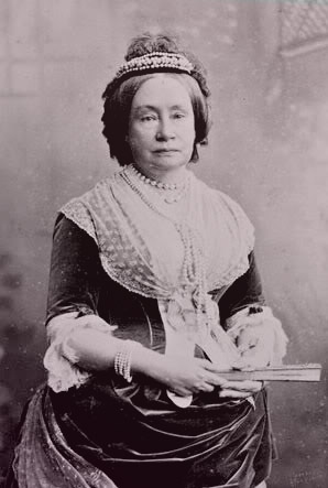 Photo of Sophie wearing a velvet and lace day dress, clutching a fan, wearing a pearl bracelet, pearl necklaces, and a small tiara.